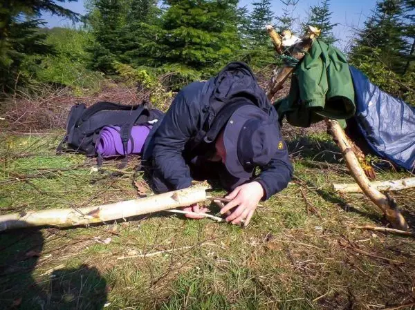 Person arbeitet an einer selbstgebauten Konstruktion aus Ästen am Boden