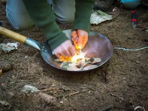 Person entzündet Material in einer Schale auf dem Boden beim Survival Training