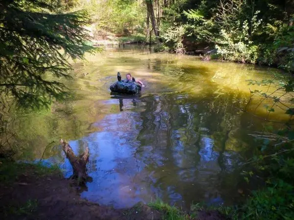 Person schwimmt mit Ausrüstung in einem klaren Gewässer umgeben von Bäumen