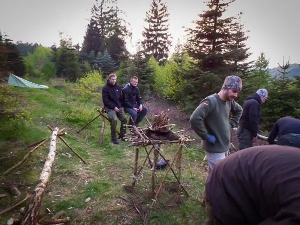 Personen sitzen und arbeiten an einer Feuerstelle im Wald beim Survival Training