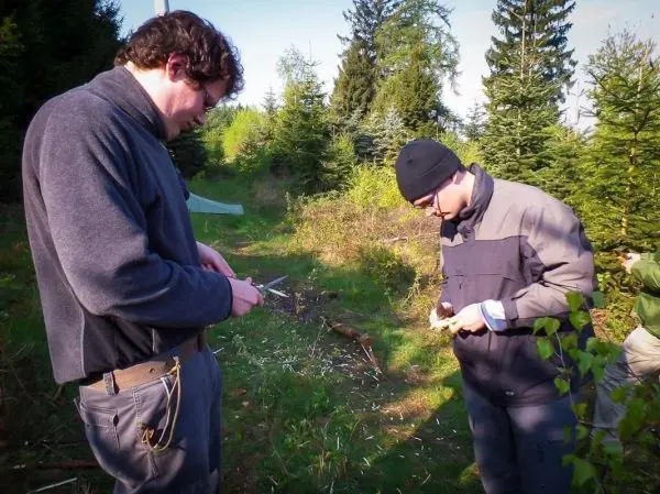 Zwei Personen bearbeiten Holzstücke mit Messern im Wald