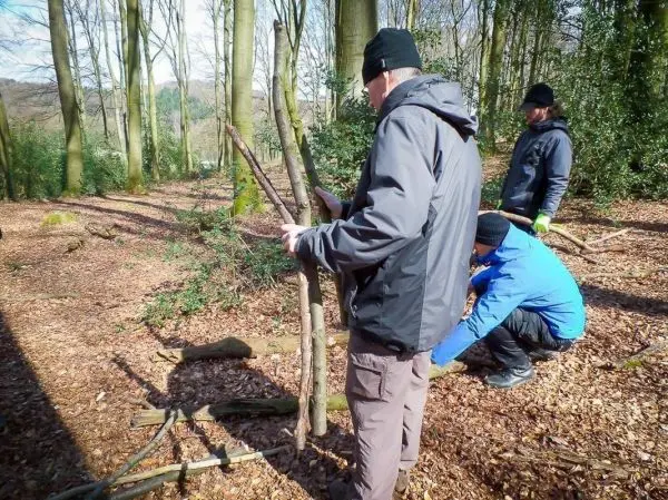 Drei Personen arbeiten an einer selbstgebauten Konstruktion aus Ästen im Wald