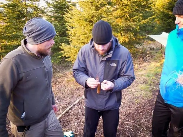 Drei Personen stehen im Wald und betrachten einen gefangenen Fisch