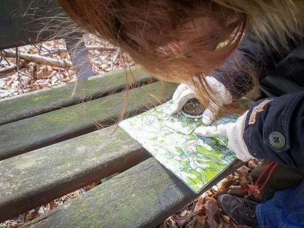 Eine Hand mit einer Lupe untersucht eine Karte auf einer Holzbank