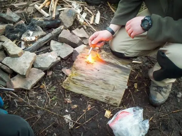 Feuerstahl entzündet Zunder auf einem Holzstück neben Steinen