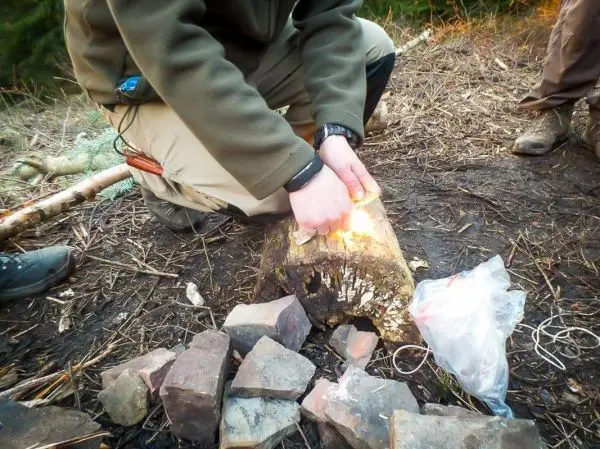 Feuerstahl erzeugt Funken auf einem Holzstück zur Zunderentzündung