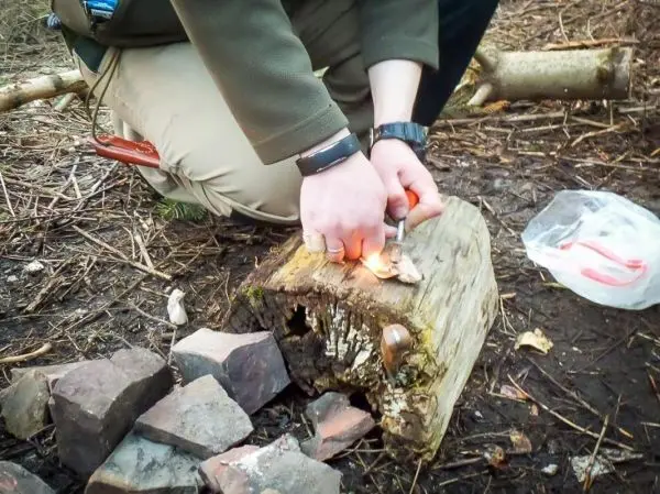 Feuerstahl erzeugt Funken auf Zunder auf einem Holzstück