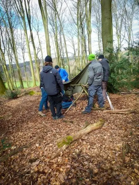 Gruppe baut Tarp-Notunterkunft zwischen Bäumen im Wald auf