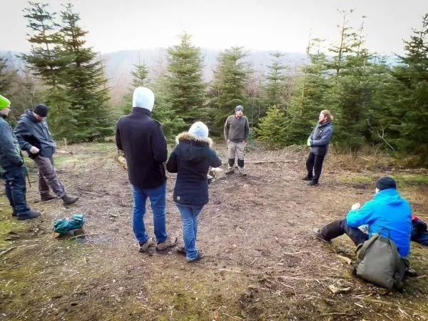 Gruppe steht im Wald und hört einem Vortragenden zu