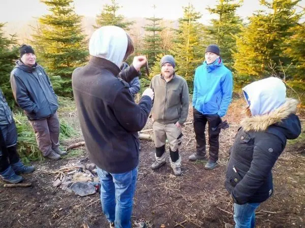 Gruppe steht um ein kleines Bodenfeuer in einem Waldgebiet