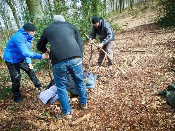 Gruppierung baut improvisierte Trage aus Ästen zur Unterstützung einer liegenden Person