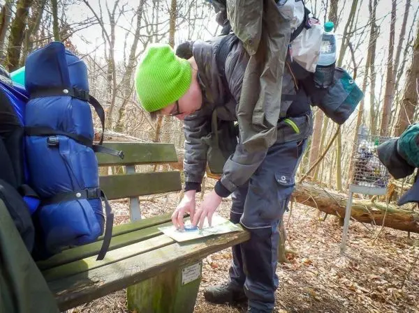 Karte wird auf einer Bank im Wald studiert, Rucksack und Wasserflasche sichtbar