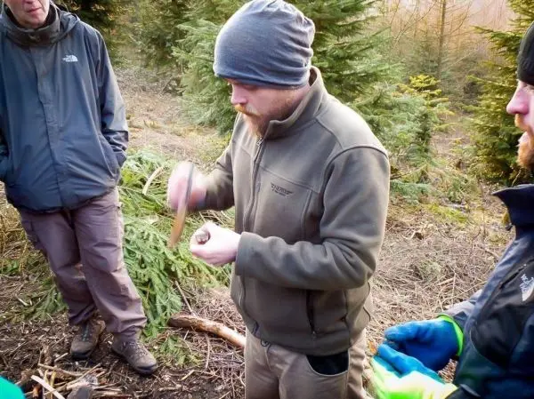 Mann bearbeitet Holzstück mit einem Messer in einem Waldgebiet