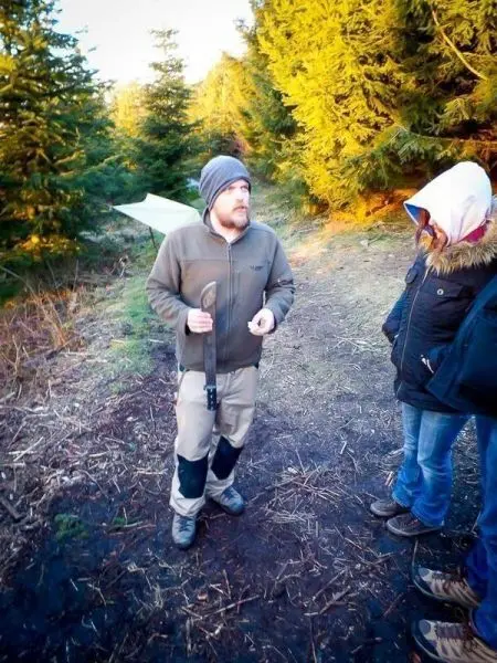 Mann erklärt etwas mit einem Messer in der Hand, zwei Personen hören zu