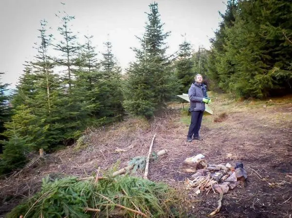 Mann hält eine Axt und steht neben einem kleinen Holzstapel im Wald