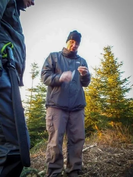 Mann hält einen kleinen Gegenstand in der Hand, umgeben von Bäumen