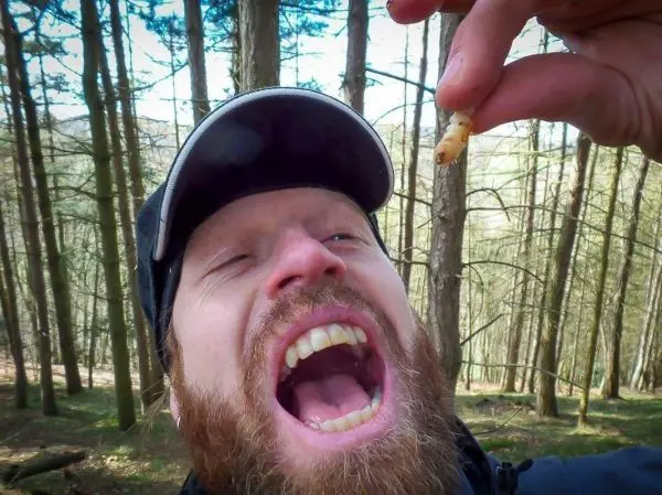 Mann hält einen Wurm in der Hand und öffnet den Mund weit