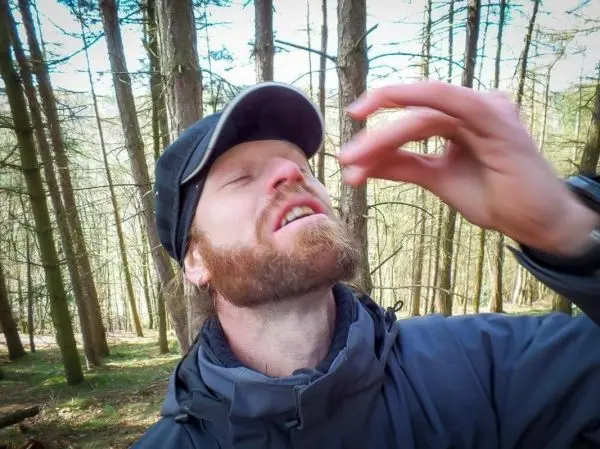 Mann mit Bart und Mütze steht im Wald und streut etwas in die Luft