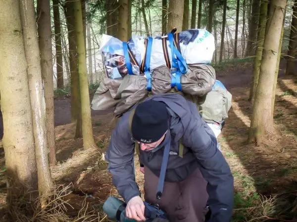 Mann mit Rucksack und improvisierter Trage in einem Waldgebiet