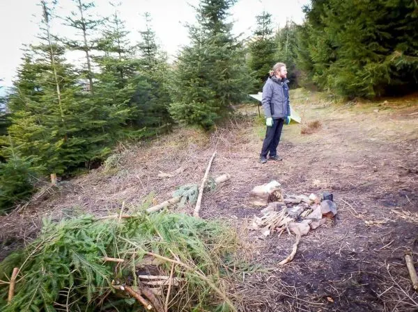 Mann steht neben einem kleinen Bodenfeuer in einem Waldgebiet