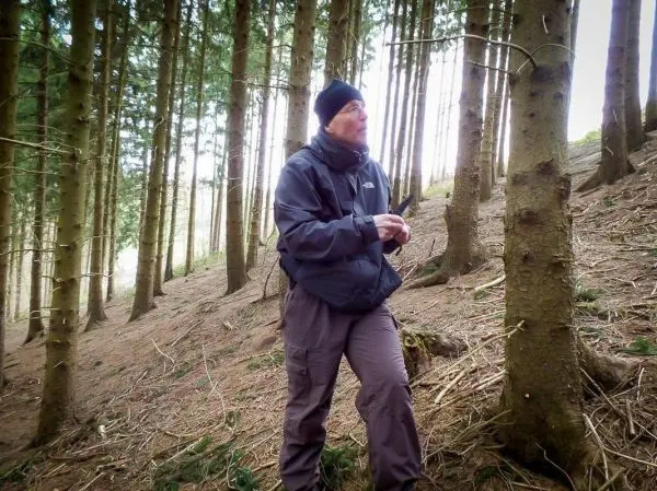 Mann steht zwischen Bäumen im Wald und hält einen Gegenstand in der Hand