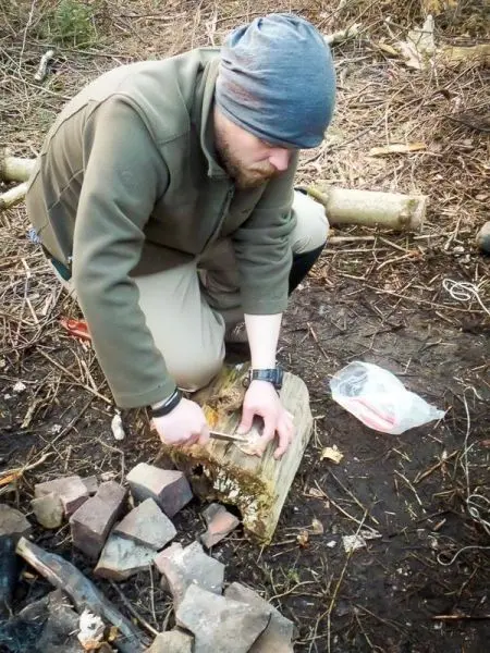 Messer schneidet Holzstück auf dem Boden neben Steinen und Zunder