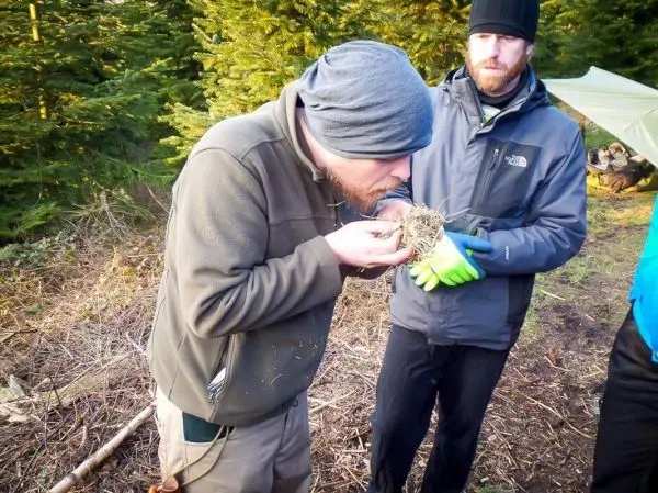 Person bläst auf ein Nest aus trockenem Gras und Zweigen