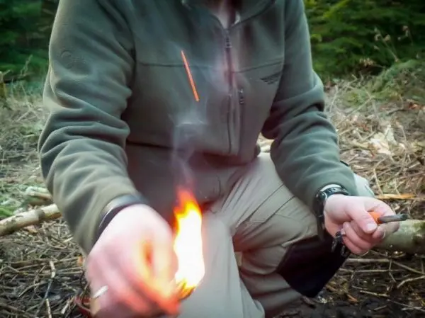 Person entzündet Feuer mit einem Zündholz beim Überlebenstraining