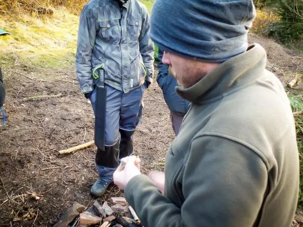 Person hält ein Stück Papier über einem Holzstapel beim Überlebenstraining