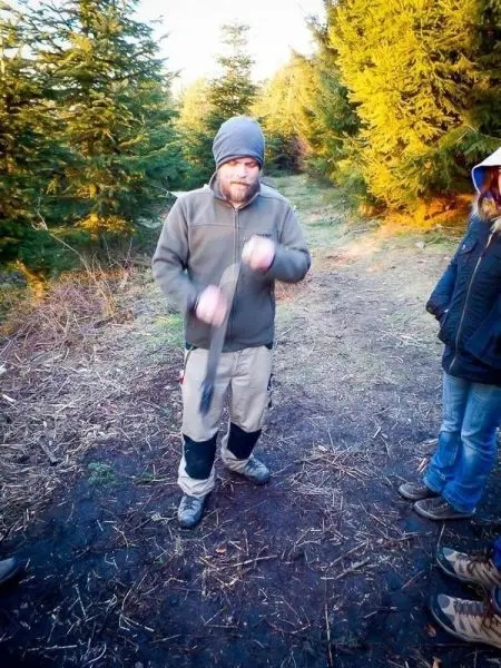 Person hält ein Werkzeug und zeigt eine Technik im Wald