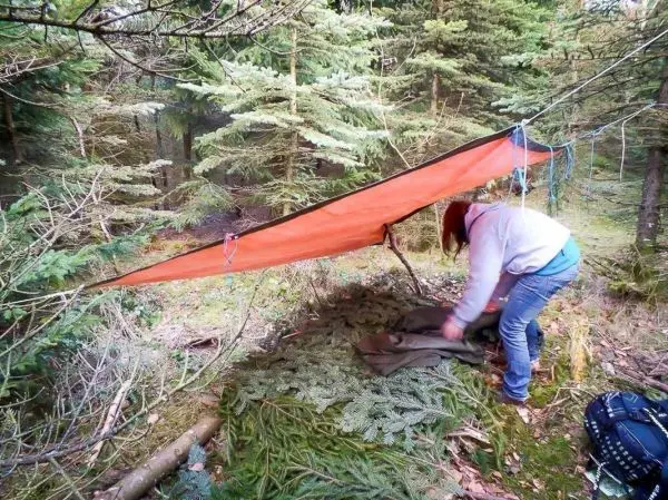 Person richtet eine Plane unter Bäumen aus beim Überlebenstraining