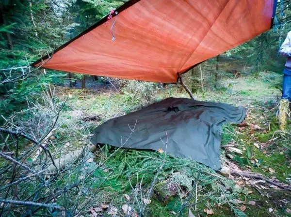 Tarp-Notunterkunft hängt über einer improvisierten Liege aus einer Decke