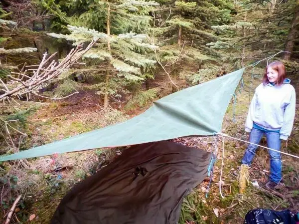 Tarp-Notunterkunft ist zwischen Bäumen gespannt, darunter liegt eine Decke