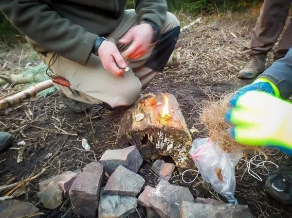 Zunder glimmt auf einem Holzstück, während eine Hand Funken erzeugt