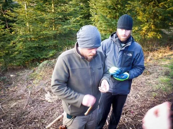 Zwei Personen arbeiten im Wald mit einem Messer und einem kleinen Gegenstand