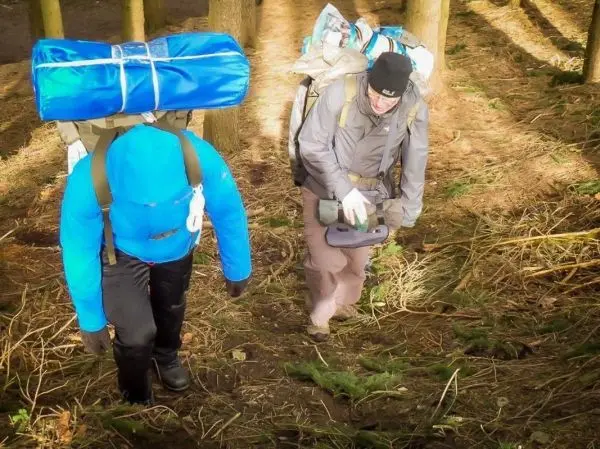 Zwei Personen tragen Rucksäcke und gehen einen steilen Waldweg hinauf