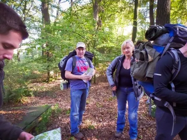 Drei Personen mit Rucksäcken stehen im Wald und betrachten eine Karte