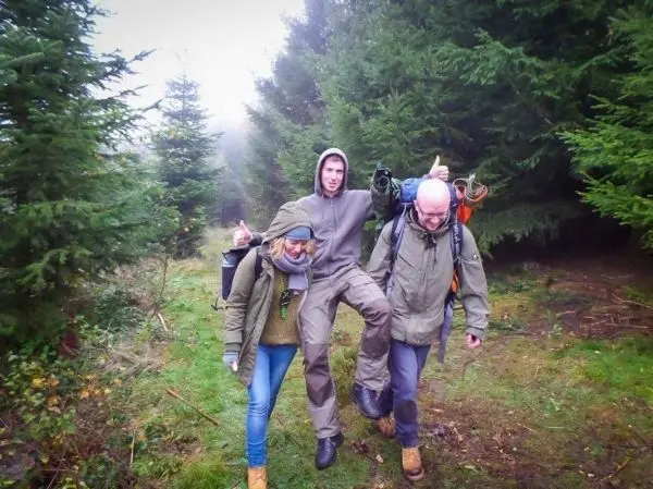 Drei Personen wandern auf einem Waldweg zwischen hohen Bäumen