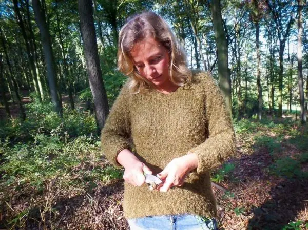 Frau bearbeitet ein Stück Holz mit einem Messer im Wald