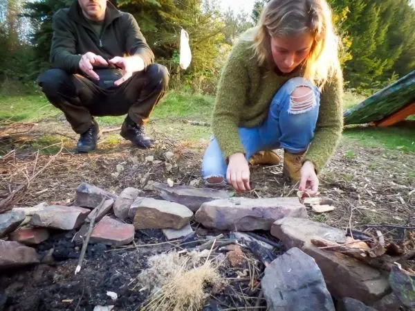 Frau bereitet Zunder im Feuerkreis aus Steinen vor
