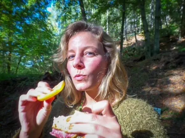 Frau hält ein Sandwich und eine gelbe Frucht in der Hand, im Wald