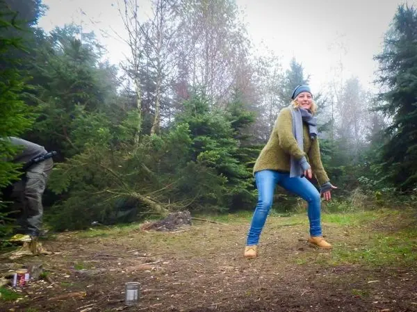 Frau in grüner Jacke und blauer Mütze steht in einem Waldgebiet