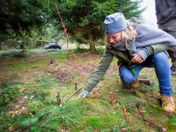 Frau kniet im Wald und untersucht Äste auf dem Boden
