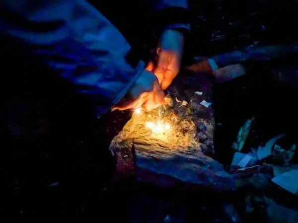 Funken fliegen auf Zunder, während Hände Feuerstahl nutzen