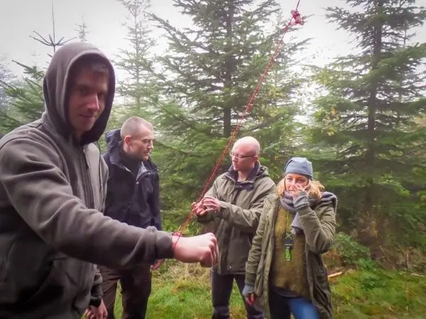 Gruppierung von vier Personen in einem Wald, eine Person hält ein Seil