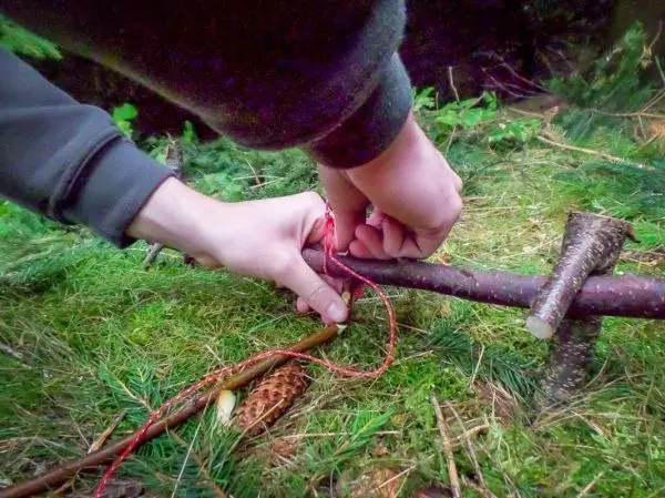 Hände binden eine Schnur um einen Holzstock zur Konstruktion einer Falle