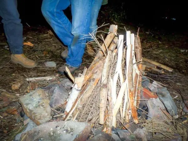 Holzstapel auf Steinen, Personen stehen daneben beim Überlebenstraining