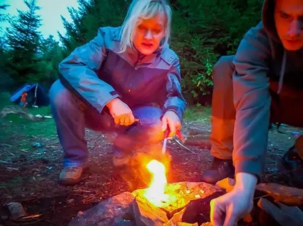 Kleine Flamme brennt in einem Steinkreis, zwei Personen beugen sich darüber