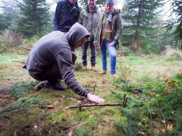 Mann baut eine Schlagfalle (Figure-Four) aus Ästen im Wald