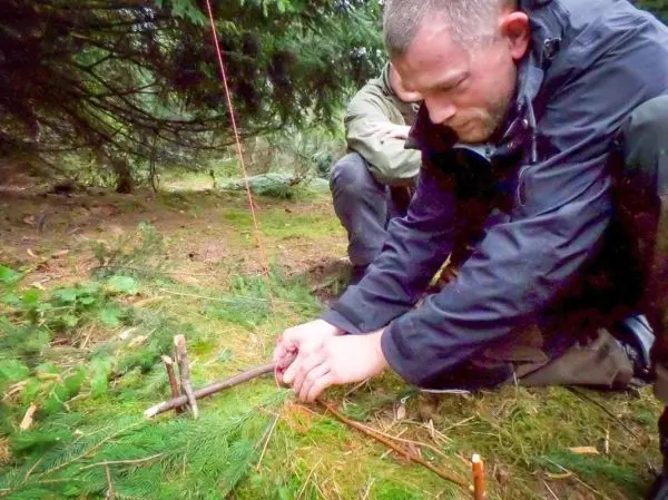 Mann baut eine Schlagfalle (Figure-Four-Falle) im Wald